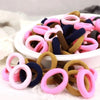 Eine Sammlung farbenfroher Nylon-Elastband-Haargummis in rosa, lila, blau und braun in einer weißen Schale.
