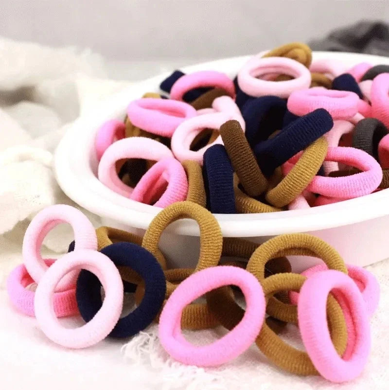 Eine Sammlung farbenfroher Nylon-Elastband-Haargummis in rosa, lila, blau und braun in einer weißen Schale.