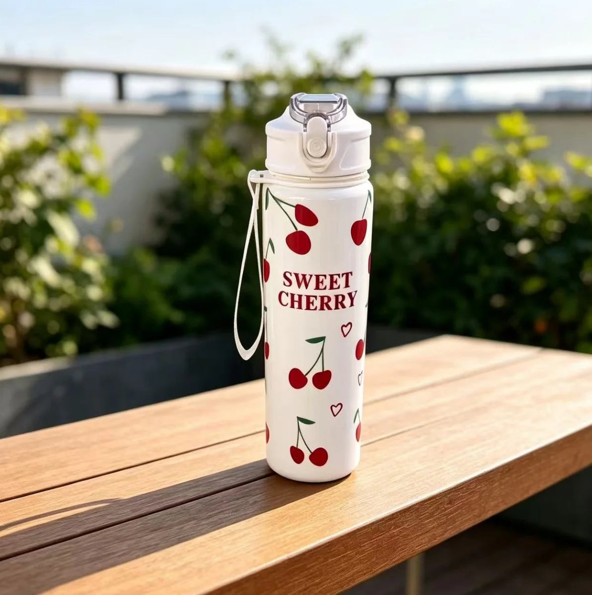 A white reusable water bottle with a silver cap and a design featuring red cherries and a heart.