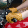 A close-up of a hand wearing tan leather motorcycle riding gloves gripping a black component on a red motorcycle.