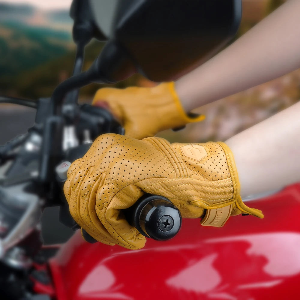 A close-up of a hand wearing tan leather motorcycle riding gloves gripping a black component on a red motorcycle.