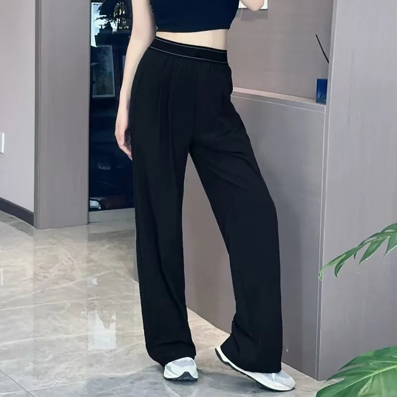 A woman wearing black loose sports yoga pants and a black top standing indoors.