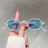 A hand holds a pair of clear-framed blue-tinted oval sunglasses against a light background.