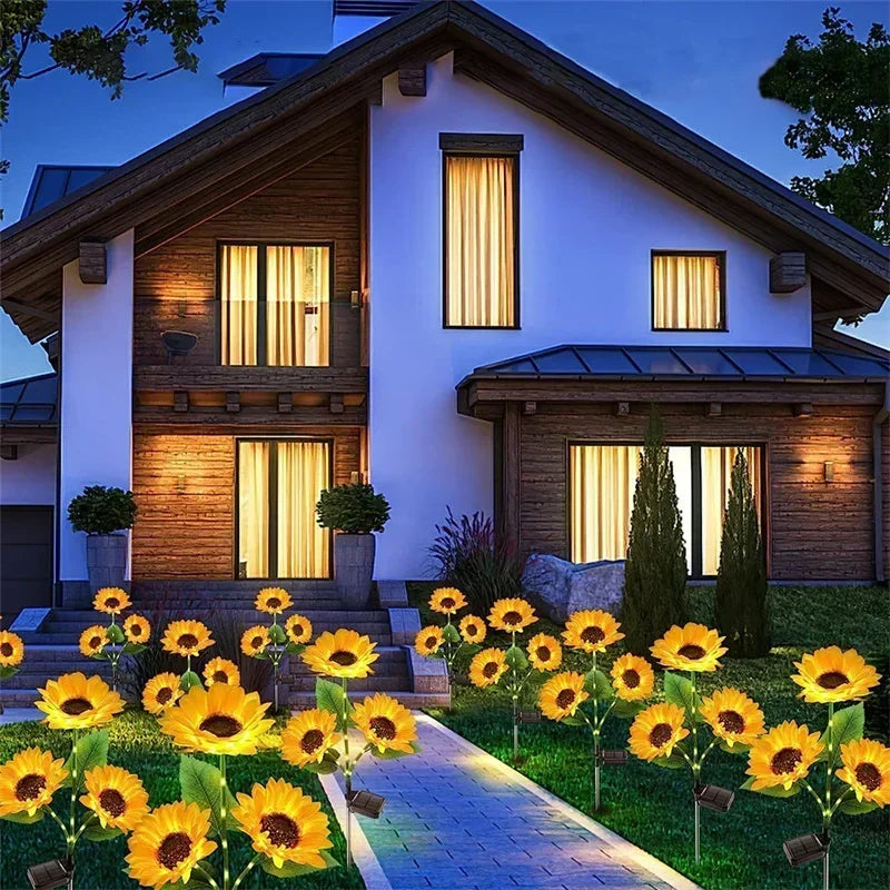 A house exterior at dusk featuring yellow sunflower plants and illuminated stake lights in the garden.