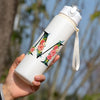 A hand holds a white insulated straw tumbler decorated with floral designs outdoors.