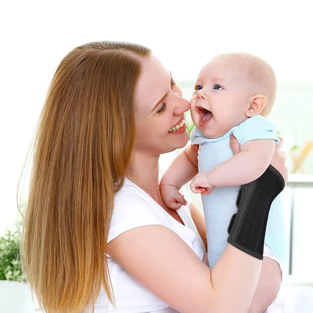 A woman is holding a baby while wearing an adjustable wrist support brace for pain relief.