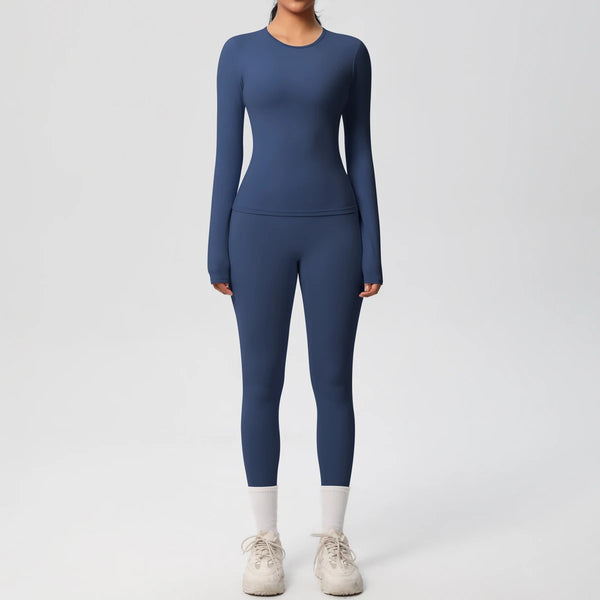 A woman wearing a navy blue long-sleeved performance yoga and gym set with white socks and gray athletic shoes.