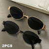 A pair of classic oval metal sunglasses in black and gold are displayed on a gray surface.