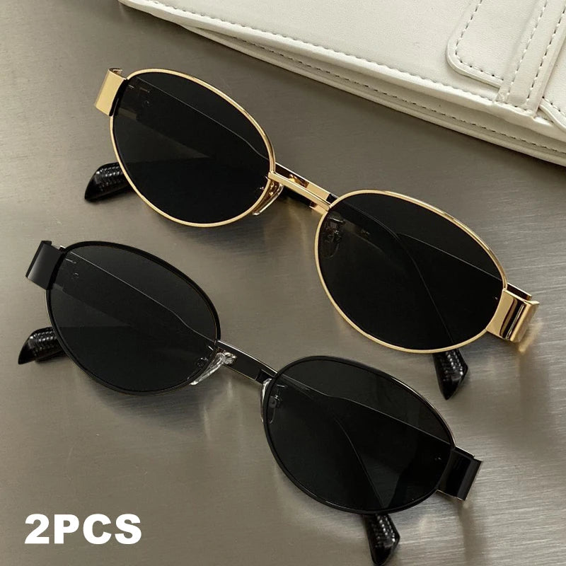 A pair of classic oval metal sunglasses in black and gold are displayed on a gray surface.