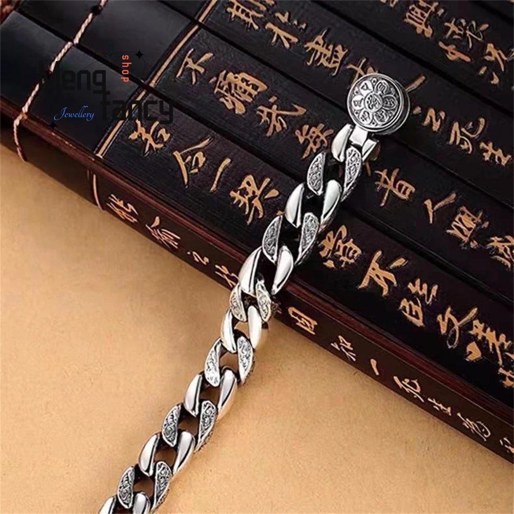 A silver mantra charm bracelet with a textured link chain and a round charm is displayed on a wooden box.