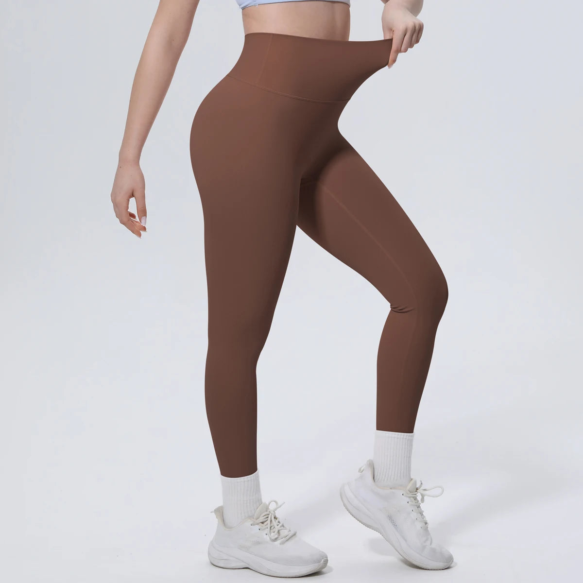 A model wearing high-waisted brown quick-drying yoga leggings and white sneakers.