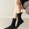 Gros plan de chaussettes noires tricotées portées sur les jambes d'une personne, associées à un tissu gris.