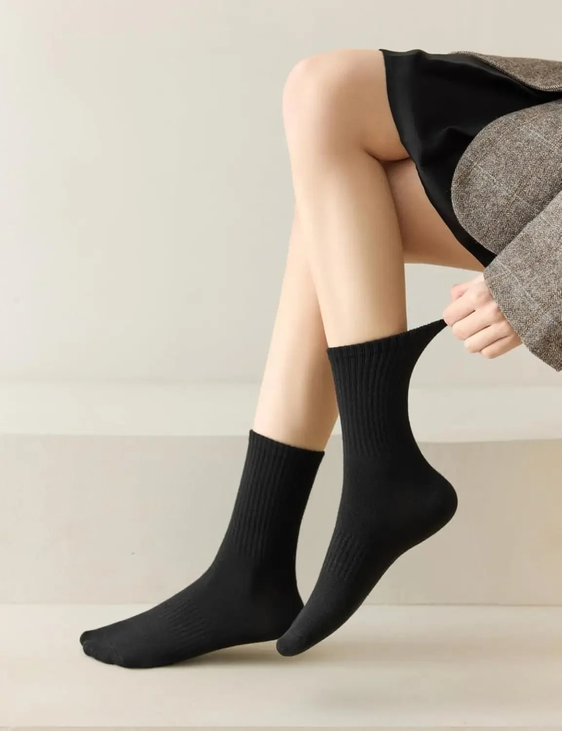 Gros plan de chaussettes noires tricotées portées sur les jambes d'une personne, associées à un tissu gris.