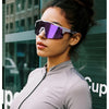 A woman wearing purple polarized sunglasses and a gray athletic shirt against a modern glass building.
