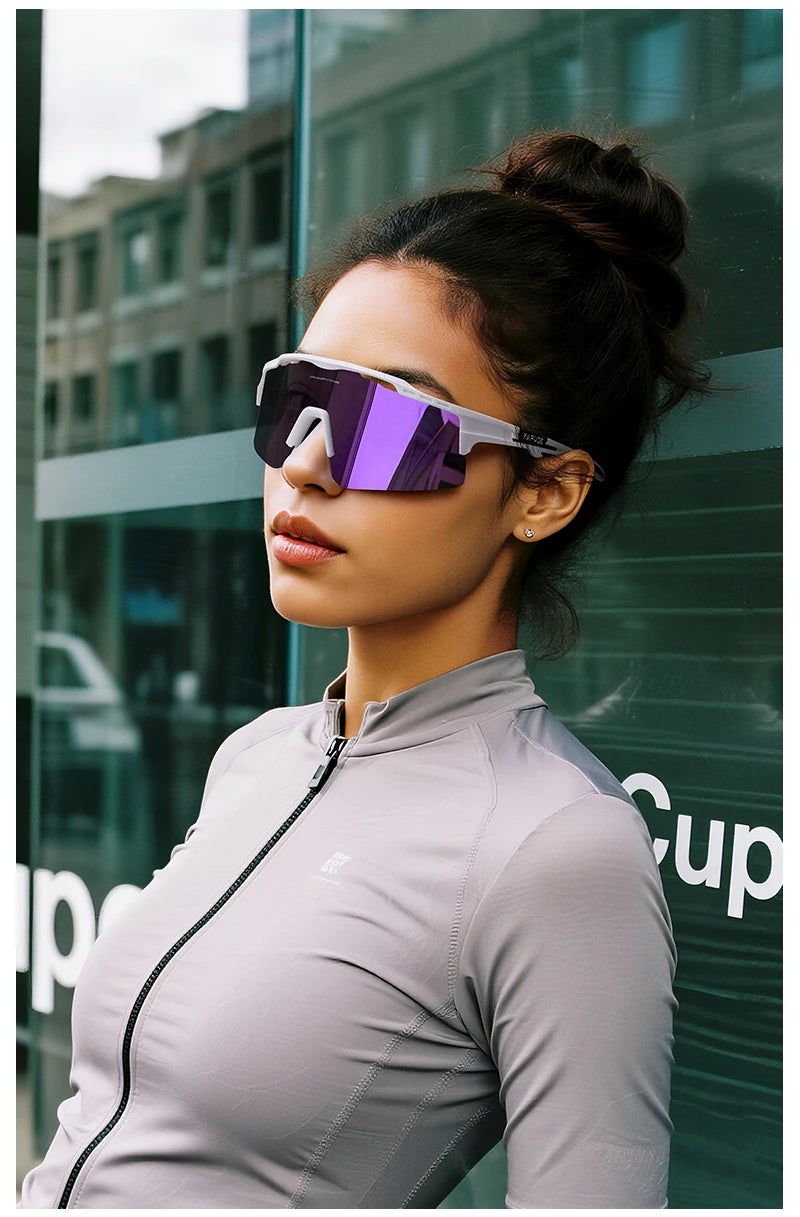 A woman wearing purple polarized sunglasses and a gray athletic shirt against a modern glass building.