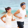 A woman and a man are running on a beach, both wearing sports headbands.