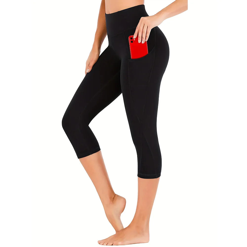 Leggings de yoga capri negros de talle alto con bolsillos de costura roja, usados por una persona.