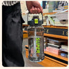 A hand holds a clear insulated sports water bottle with a yellow cap and straw, placed on a wooden shelf.