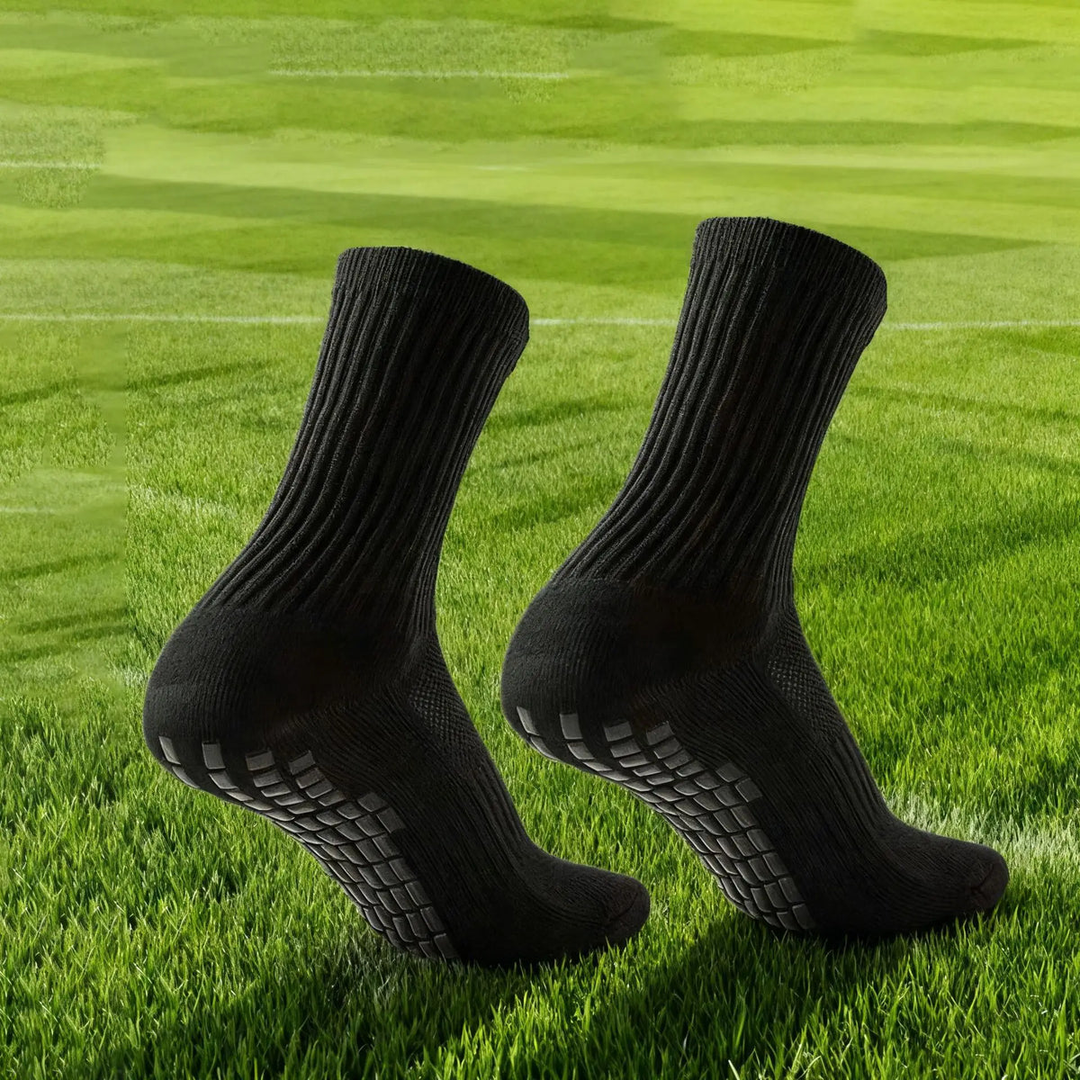 Une paire de chaussettes de football en silicone antidérapantes noires posées sur de l'herbe verte.