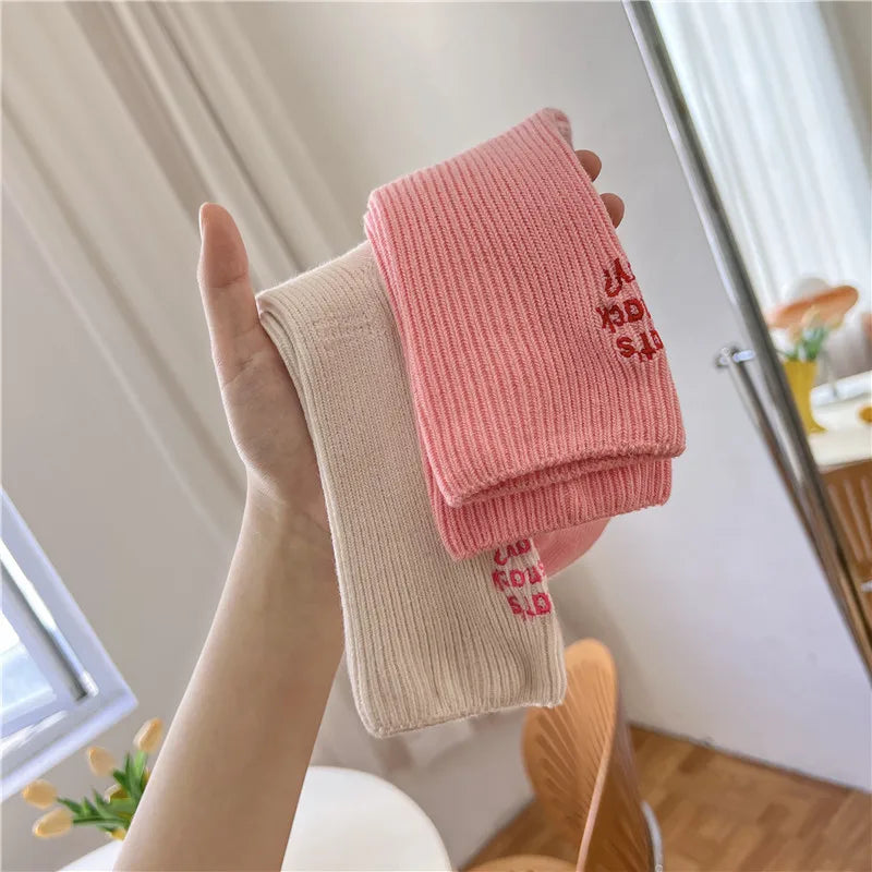 A hand holds a pink embroidered cotton sock against a bright window background.