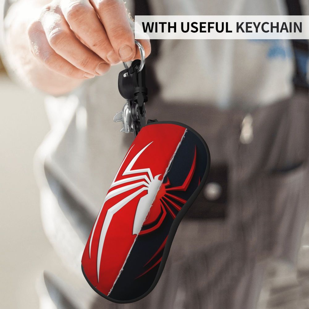 A red and black spider web shaped eyeglass pouch attached to a keychain, held by a person.