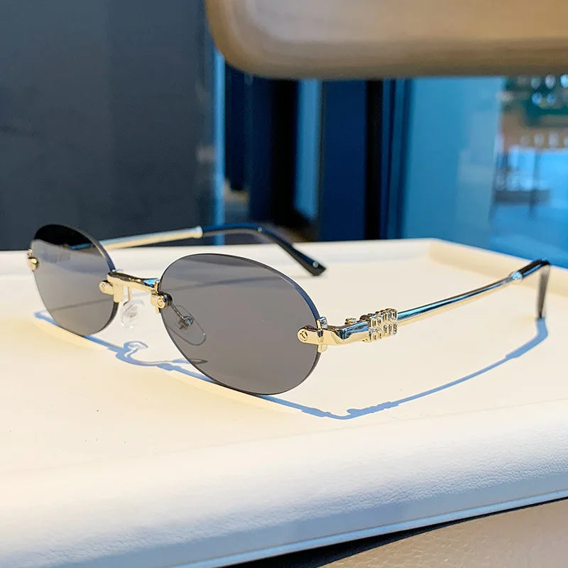 Rimless oval gradient sunglasses with gold-toned metal frame resting on a white surface.
