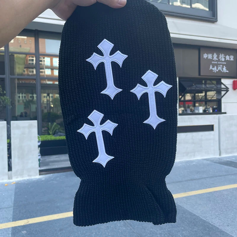 A black tactical knit balaclava beanie hat is held up against a modern building exterior.