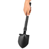 A hand is holding a black foldable multi-tool shovel with a serrated blade.