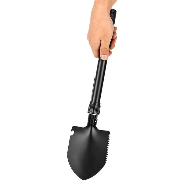 A hand is holding a black foldable multi-tool shovel with a serrated blade.