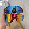 A hand holds a pair of mirrored cycling sunglasses with iridescent blue and orange lenses against a white wall.