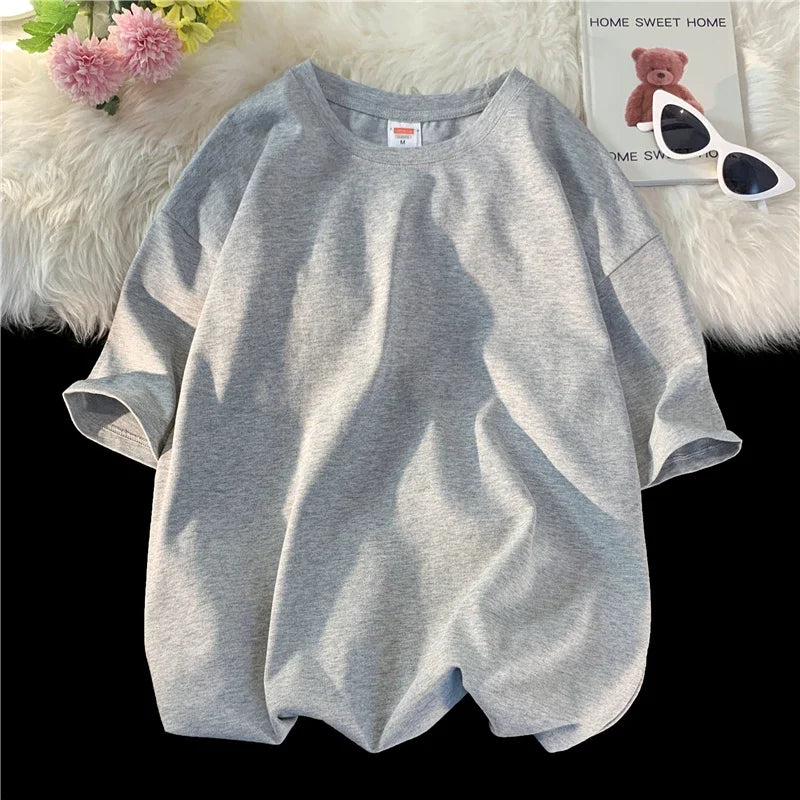 Helles graues, oversized Baumwoll-T-Shirt einer Frau auf einer weißen, flauschigen Oberfläche.