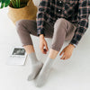 Une personne portant une chemise et un pantalon à carreaux, assise, montrant des chaussettes grises de type crew.
