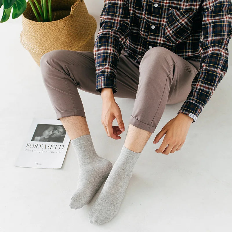 Une personne portant une chemise et un pantalon à carreaux, assise, montrant des chaussettes grises de type crew.