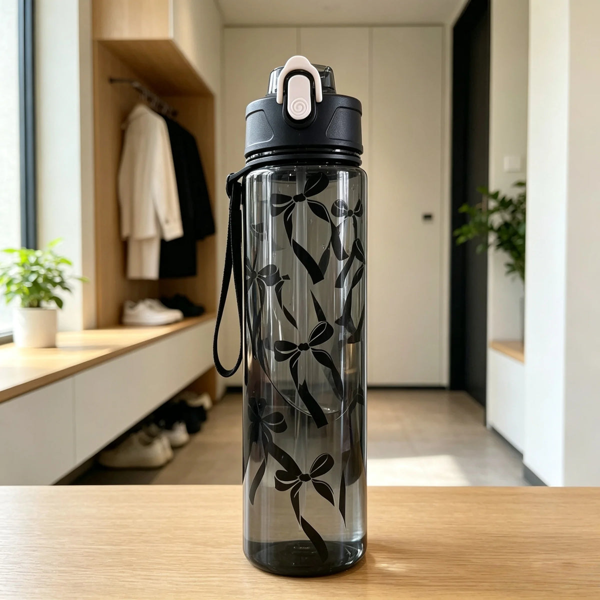 A clear reusable water bottle with a black lid and a pattern of black bows, sitting on a wooden table.