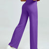 A woman is modeling high waisted purple yoga pants with a white top and white sneakers.
