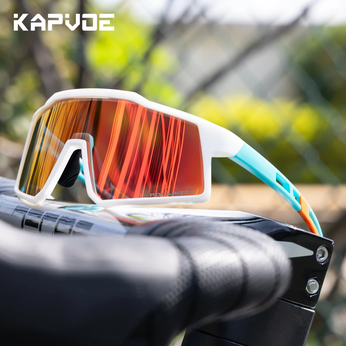 A pair of white and orange polarized sports sunglasses resting on a black bicycle handlebar.