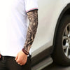 A person wearing a white shirt and black pants is displaying a long-sleeved tattoo arm sleeve on their forearm.