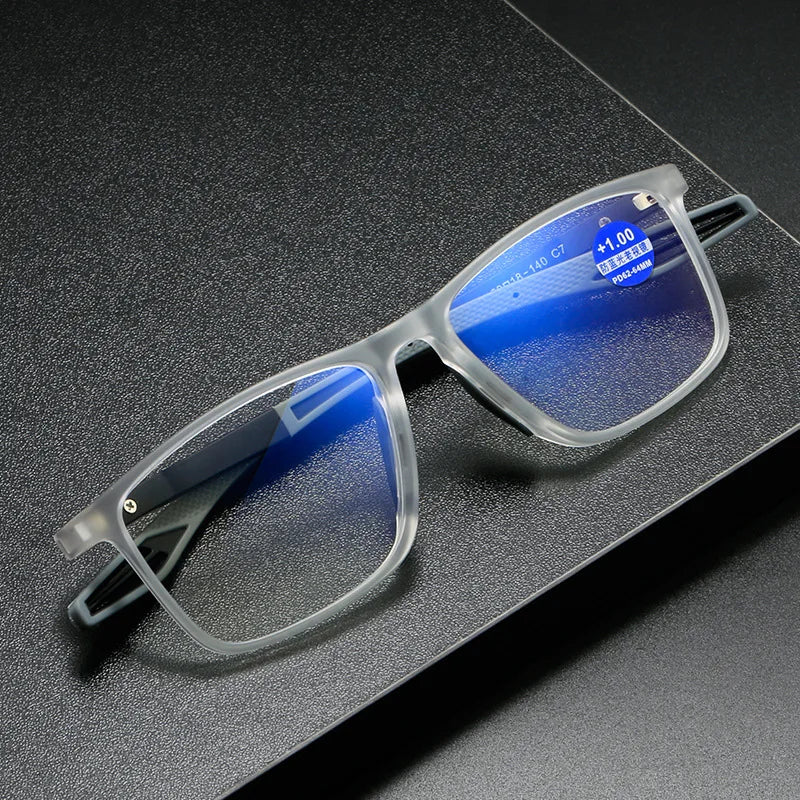 A pair of clear-framed reading glasses with blue light protection resting on a dark surface.