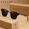 Un par de gafas de sol con marco de madera marrón sobre una caja de cartón con el logo BARCUR.