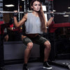 A woman exercising with a barbell, wearing gray athletic top and dark compression thigh sleeves.