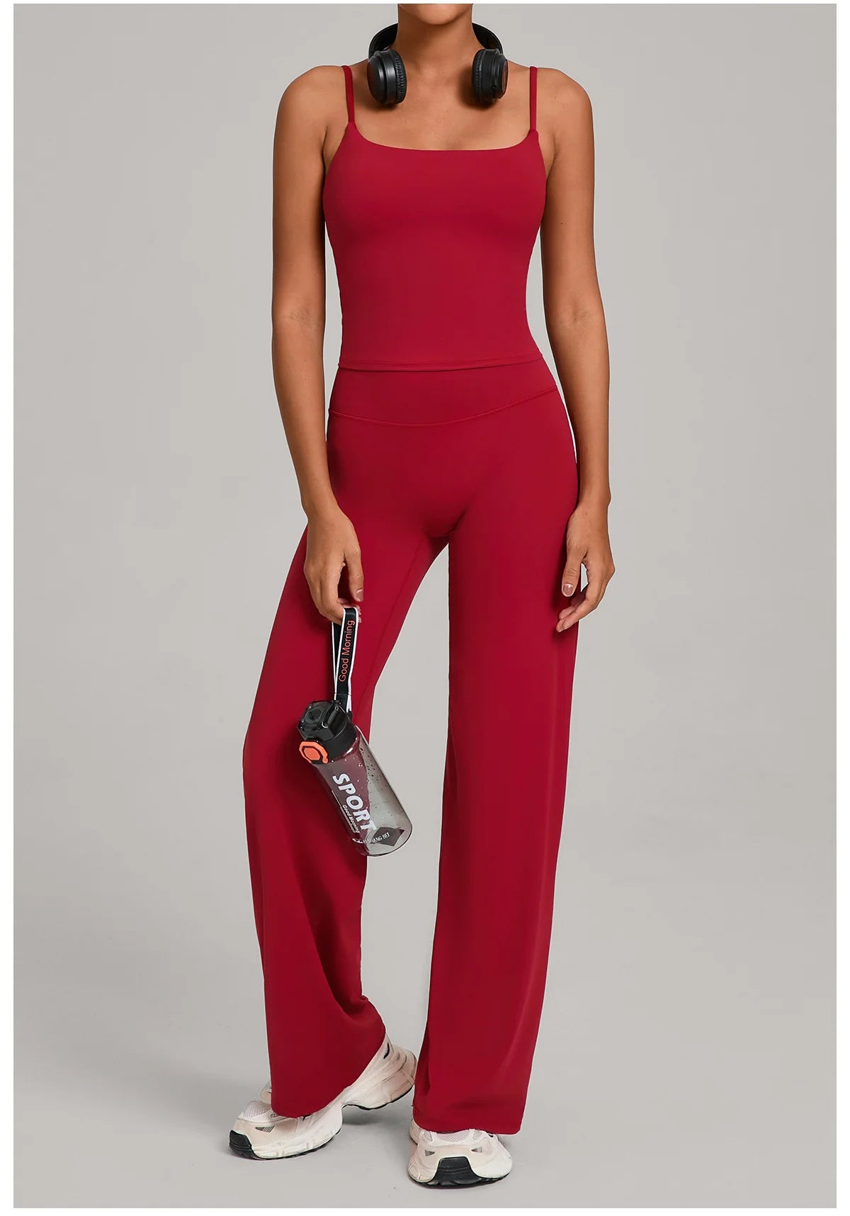 A woman wearing a red high-waist yoga and fitness tracksuit set with black headphones.