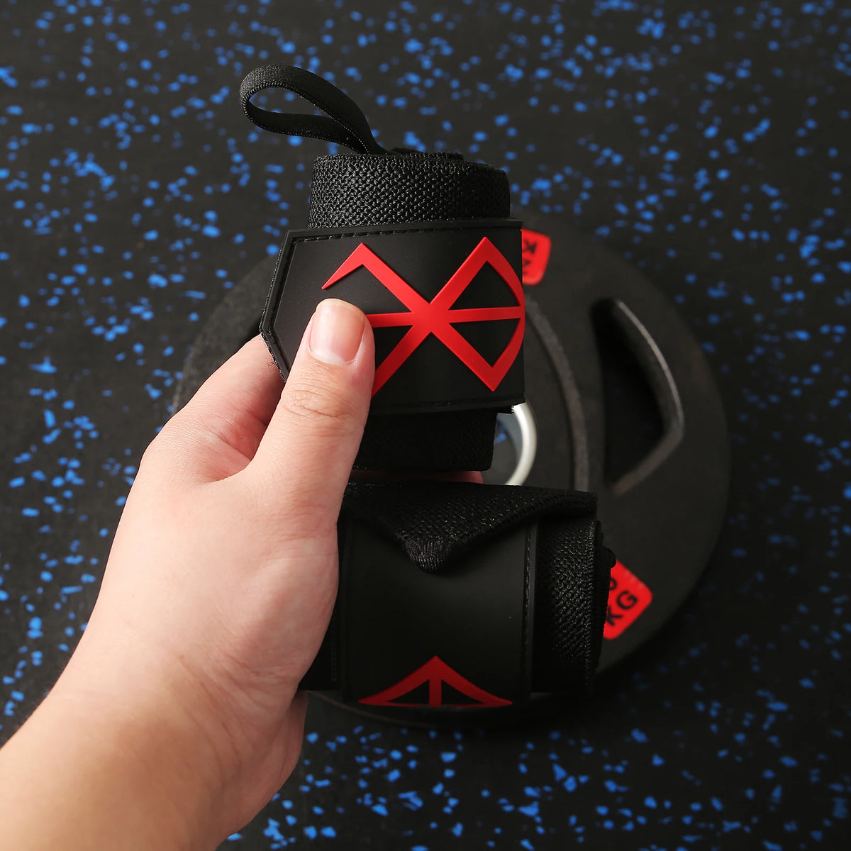 Une main tient un bandeau de poignet noir robuste avec des accents géométriques rouges sur un fond bleu foncé moucheté.