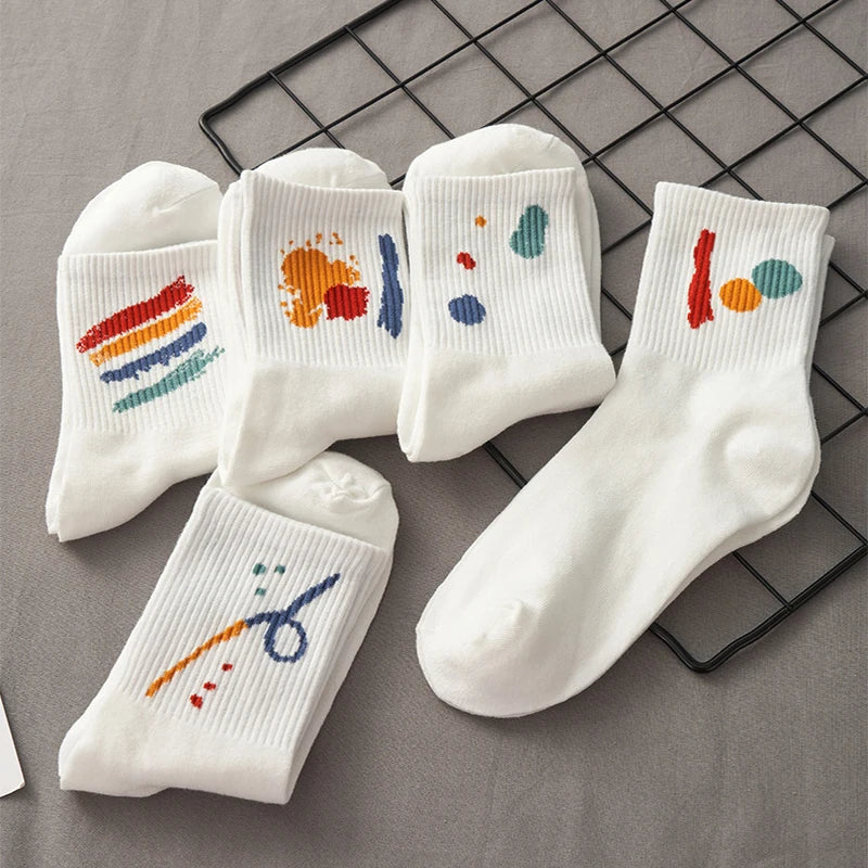 A flat lay of five white breathable cotton socks with colorful paint splatters on a black wire rack.
