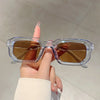 A hand holds a pair of clear plastic rectangle sunglasses with brown lenses against a light background.
