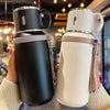 Une personne tient deux bouteilles isothermes en acier inoxydable, une noire et une blanche, contre un arrière-plan flou.