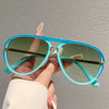 A hand holds a pair of light blue gradient sunglasses with gold accents against a plain gray background.