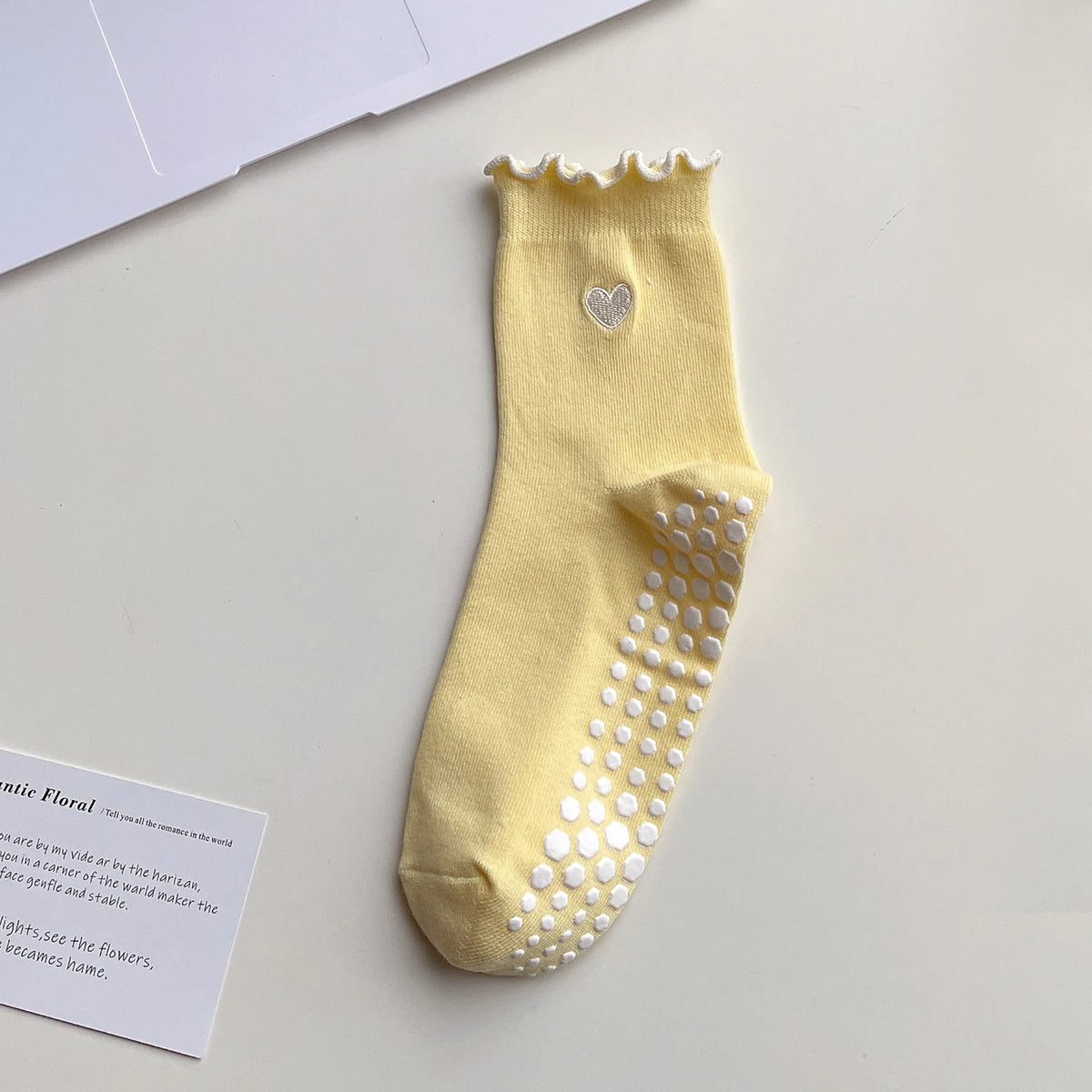 A yellow yoga sock with a ruffled cuff and a heart embroidery on the toe area.