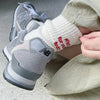 A close-up of a person's foot wearing gray embroidered cotton socks and light colored pants.