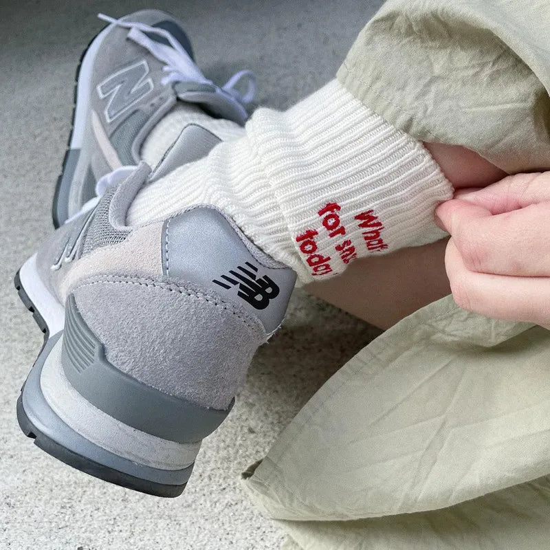 A close-up of a person's foot wearing gray embroidered cotton socks and light colored pants.