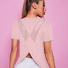 A woman wearing a light pink breathable summer yoga and fitness t-shirt with an X-shaped cutout against a pink background.